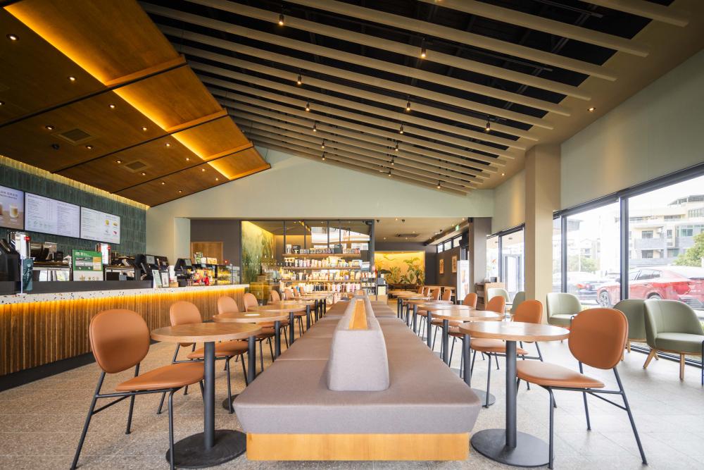 吧檯天花以斜屋頂面狀搭配木質線條延伸視覺尺度，中央長型沙發順勢向後延展，強化視覺穿透性，並結合兩側落